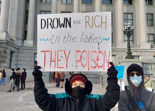 A young woman holding a white protest sign while wearing winter clothing.