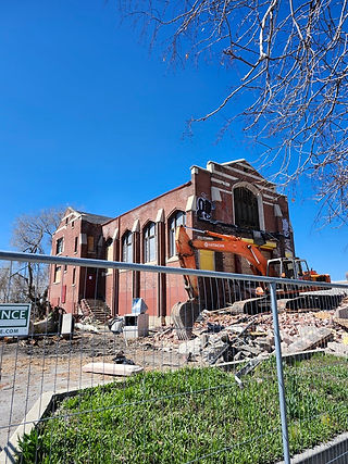 Side front view of the 5th Ward Meeting House in Salt Lake City with rubble on the front and the side surrounded by a fence.