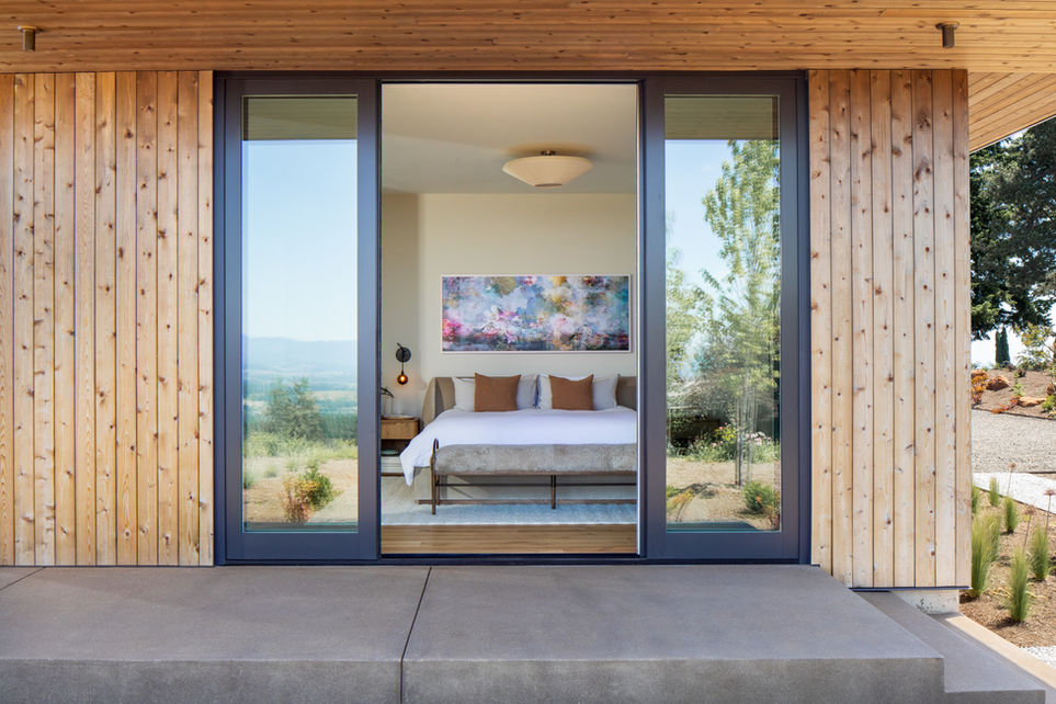 Modern Oregon bedroom with sliding glass doors opening to vineyard views, minimalist decor, and warm wood accents at Hillside House.