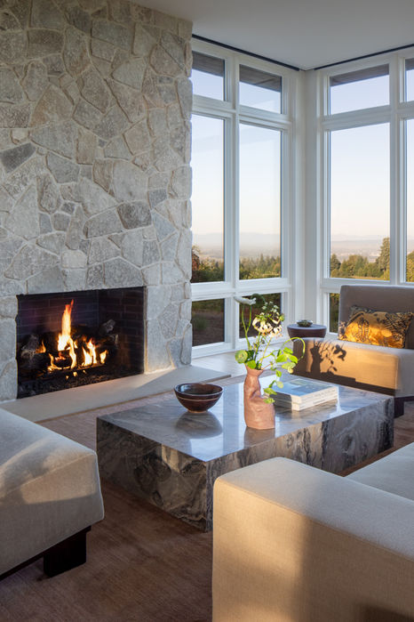 Contemporary Oregon living room with floor-to-ceiling stone fireplace, marble coffee table, and vineyard views at Hillside House.