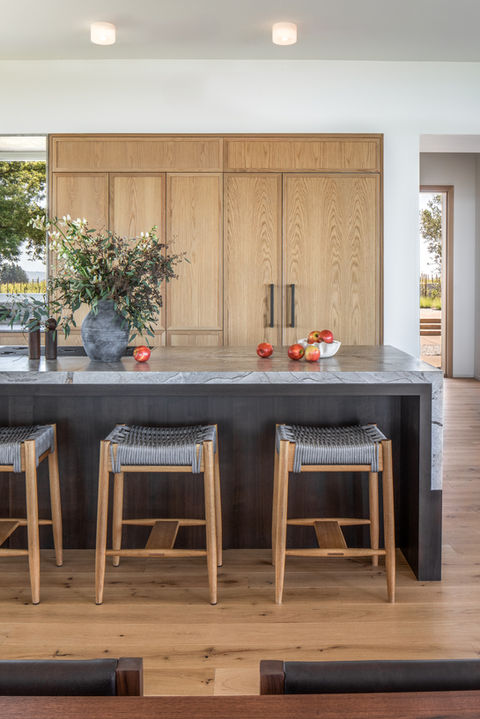 Custom Oregon home kitchen with stone island, wood cabinetry, and woven bar stools blending modern design with natural materials.