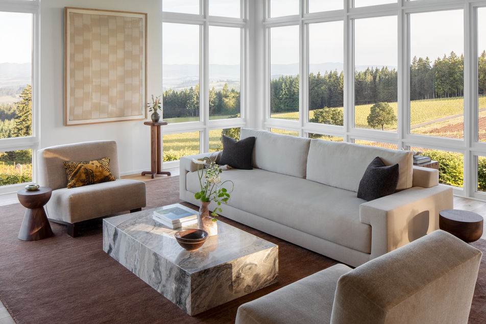 Hillside House living space with modern neutral furnishings, marble coffee table, and expansive Willamette Valley views through large windows.