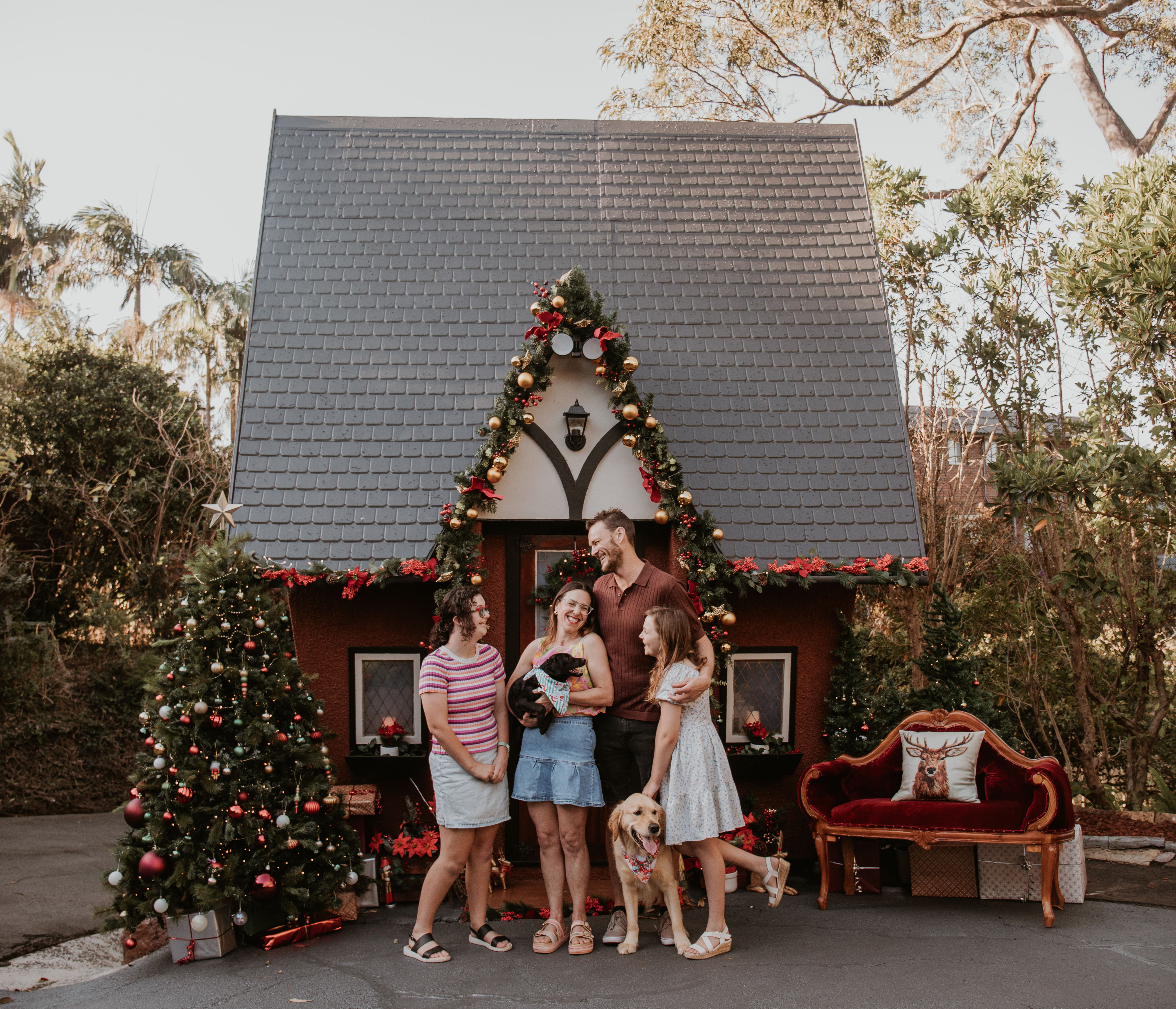 Family enjoying an outdoor Christmas mini photography session in front of a beautifully decorated cottage in Wollongong.
