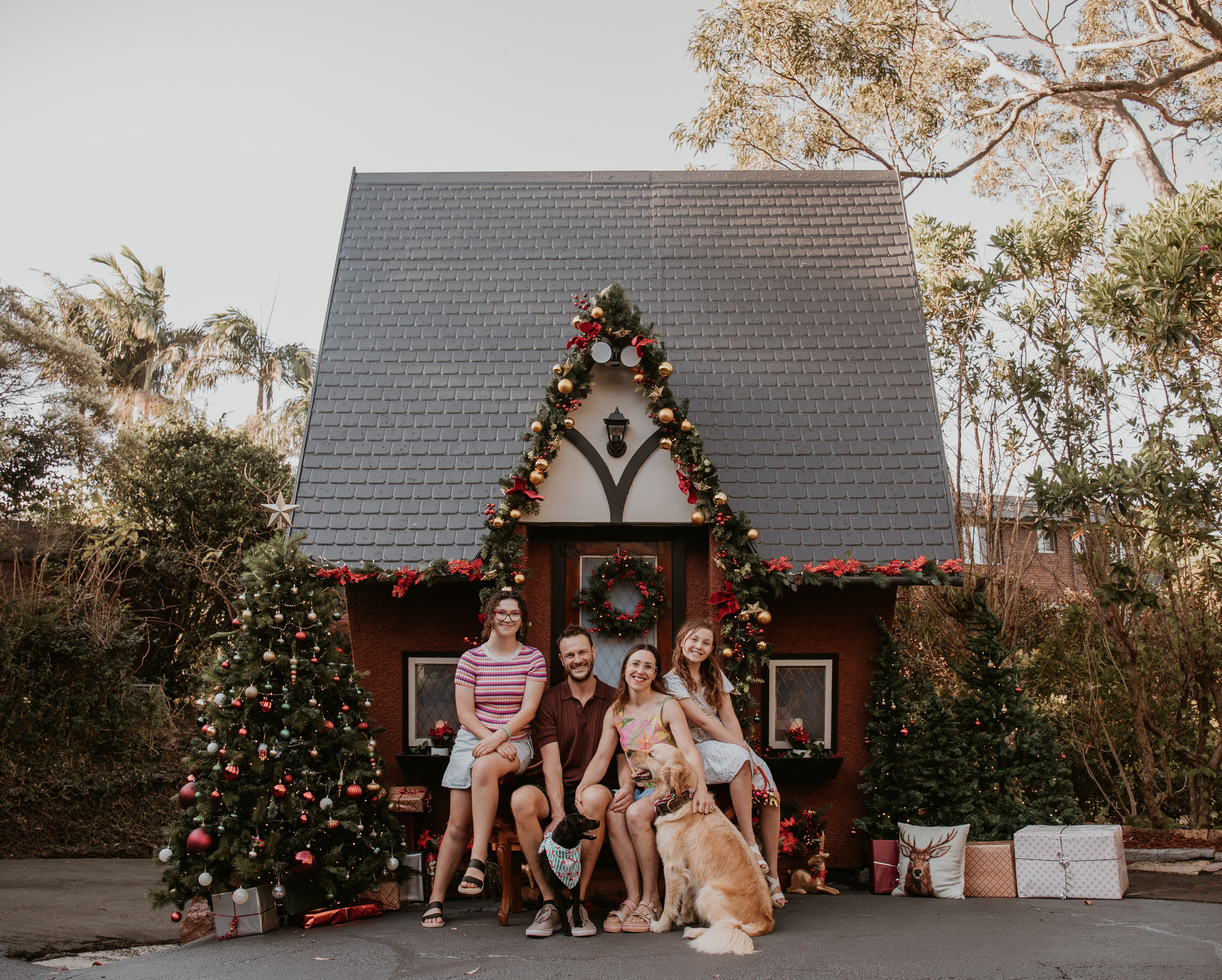 Family enjoying an outdoor Christmas mini photography session in front of a beautifully decorated cottage in Wollongong.