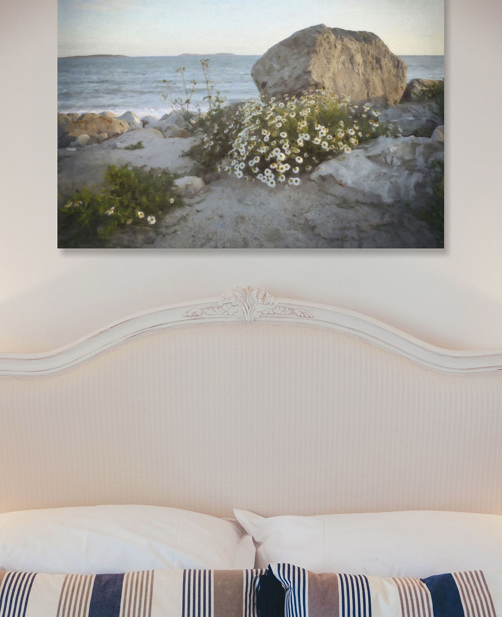 Striped cushions on a bed with a cream headboard. A seascape painting with rocks and white daisies
hangs above, creating a serene mood.