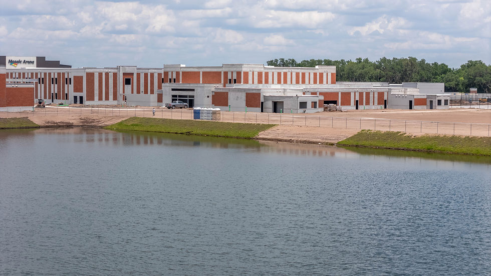 The south side of the school overlooks a tranquil pond under a cloudy sky, near the Mosaic Arena.