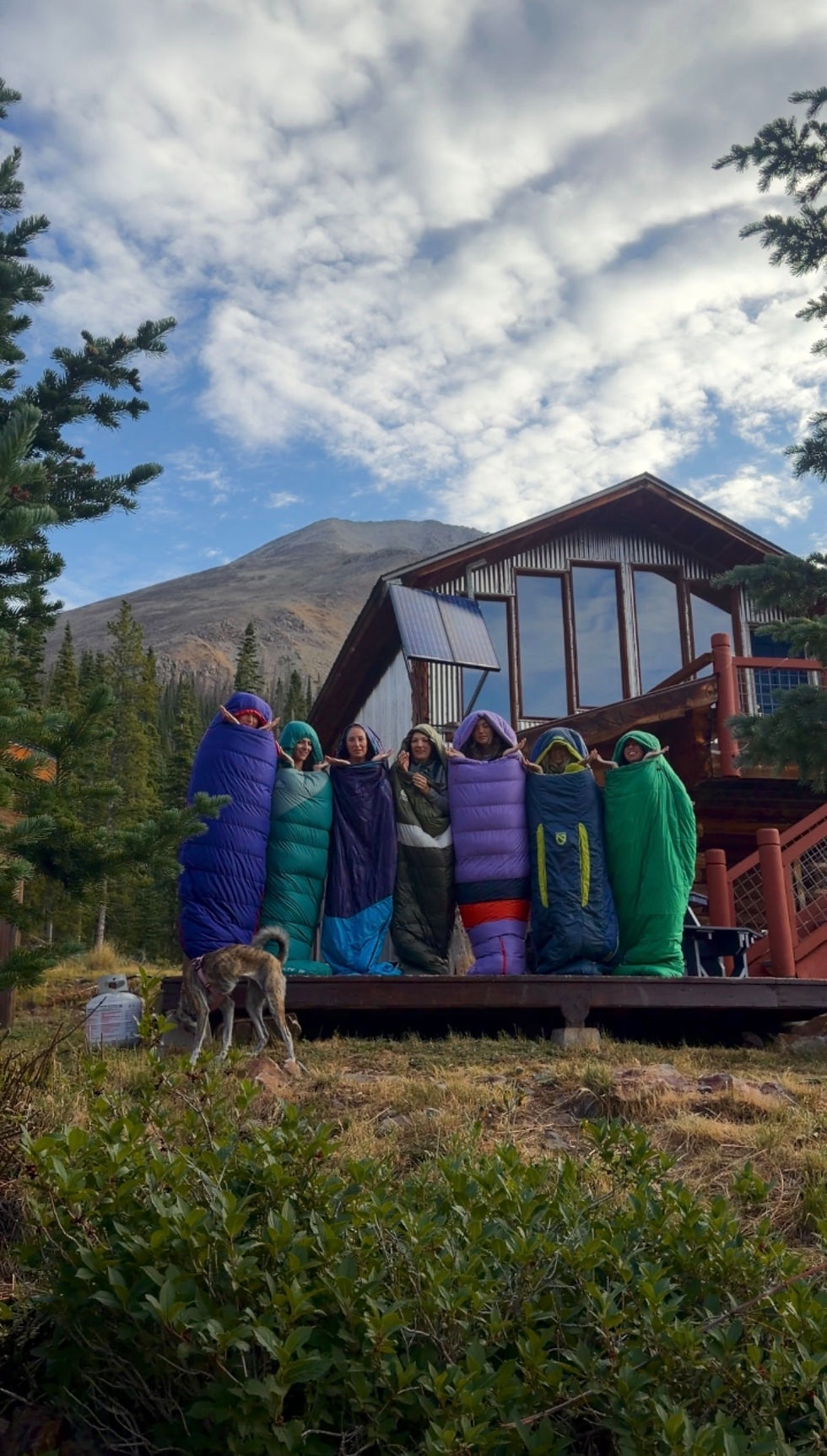 Group of women posing in sleeping bags in front of backcountry hut Lost Wonder Hut