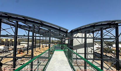 גשר הולכי רגל בבנייה, שלד פלדה מרשים תחת שמיים כחולים.