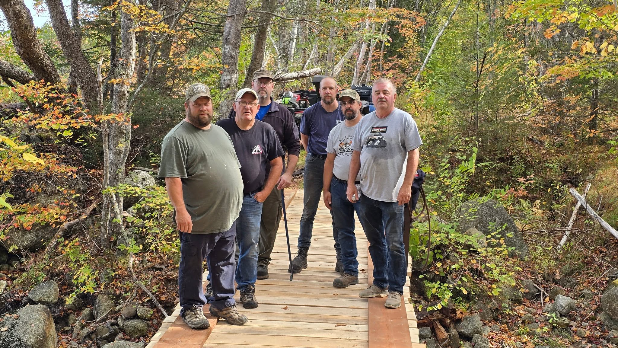 Club volunteers standing on a wooden trail bridge in the woods after maintenance work