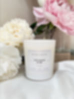 A scented candle in a white jar in front of peony flowers
