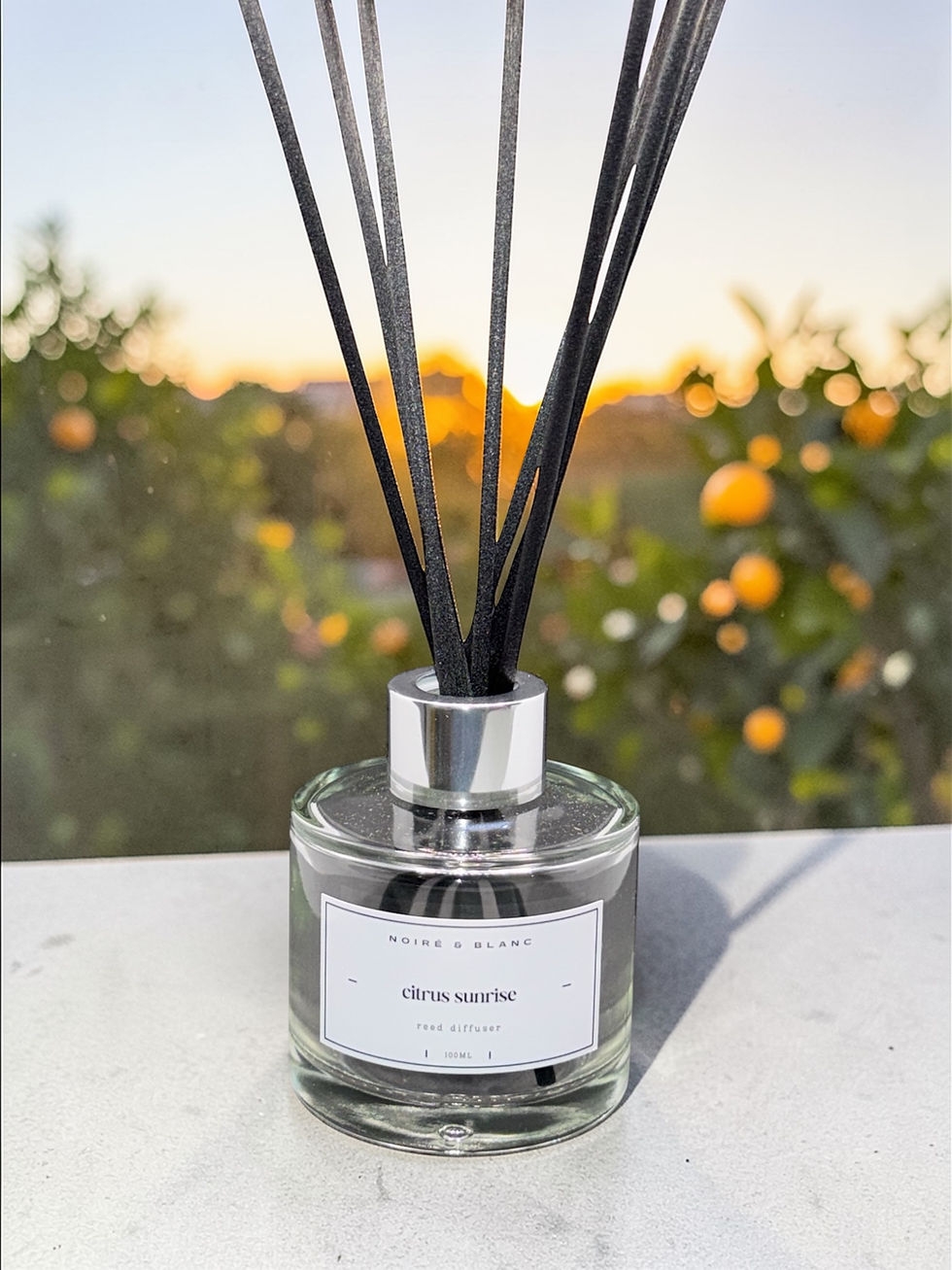 Thumbnail: A 100ml reed diffuser in front of an orchard