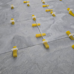 a row of yellow tile spacers on a gray Marble tile floor 
