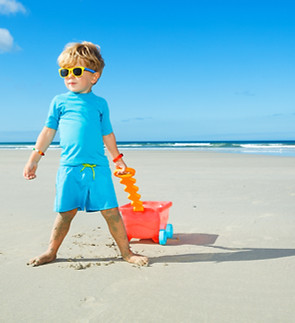 Happy little boy in sunglasses walk on the white sand beach playing with toy cart_edited.j
