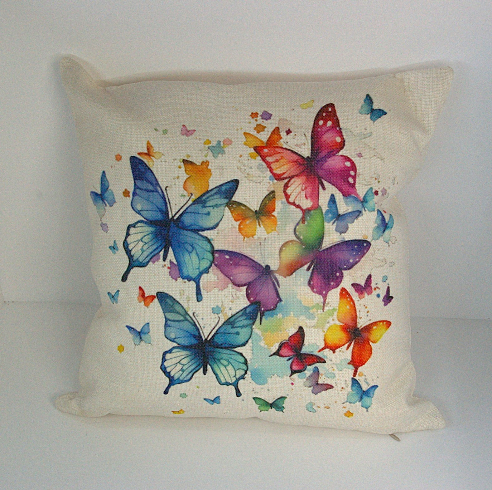 Cream linen cushion featuring watercolour swarm of multicoloured Butterflies paint splashes & drips
