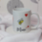 White ceramic mug with cartoon Bee with big eyes flying above "mine" black script with several red hearts in different sizes