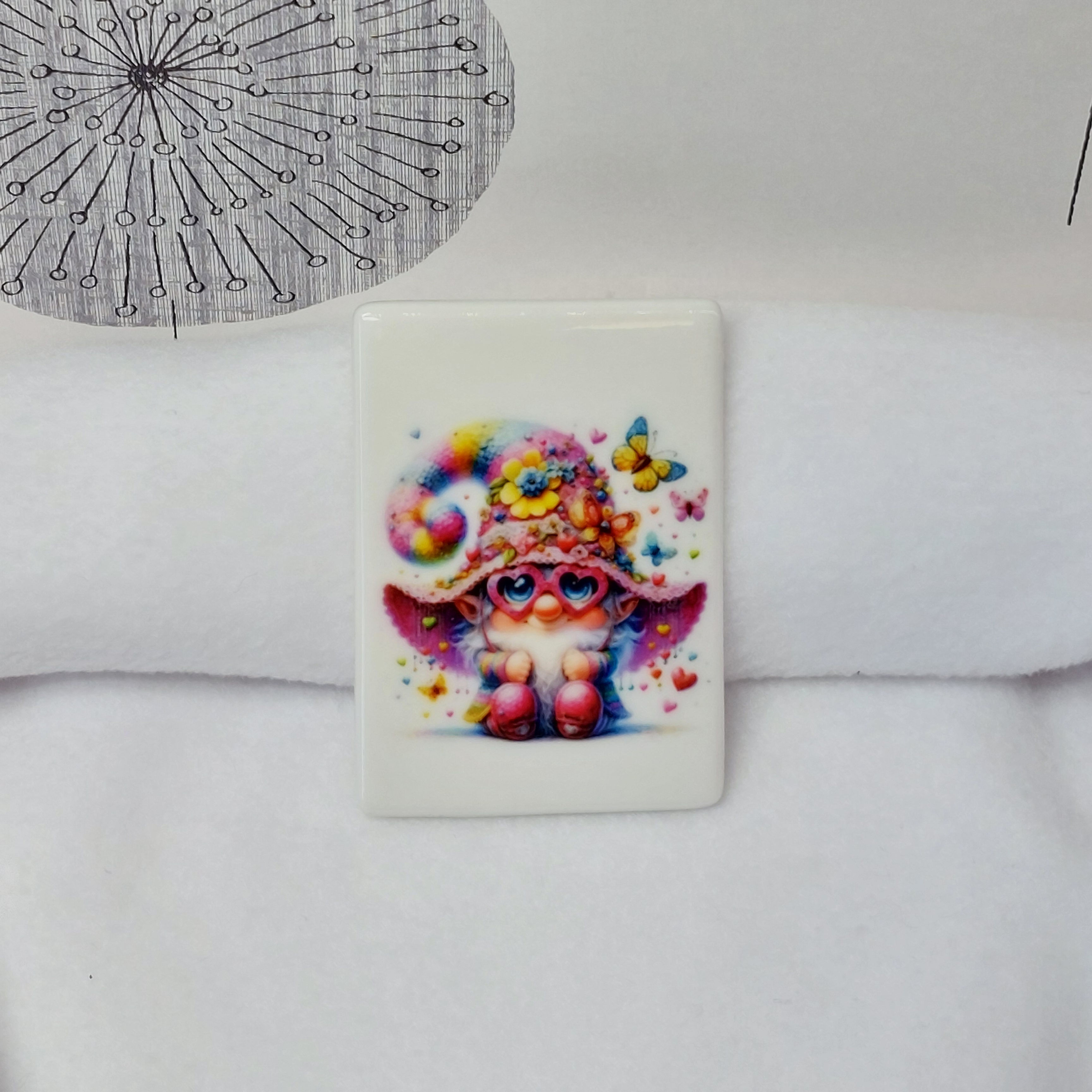 illustration of a gnome with a pink heart sunglasses and rainbow hat with butterflies, hearts and flowers on a rectangular ce