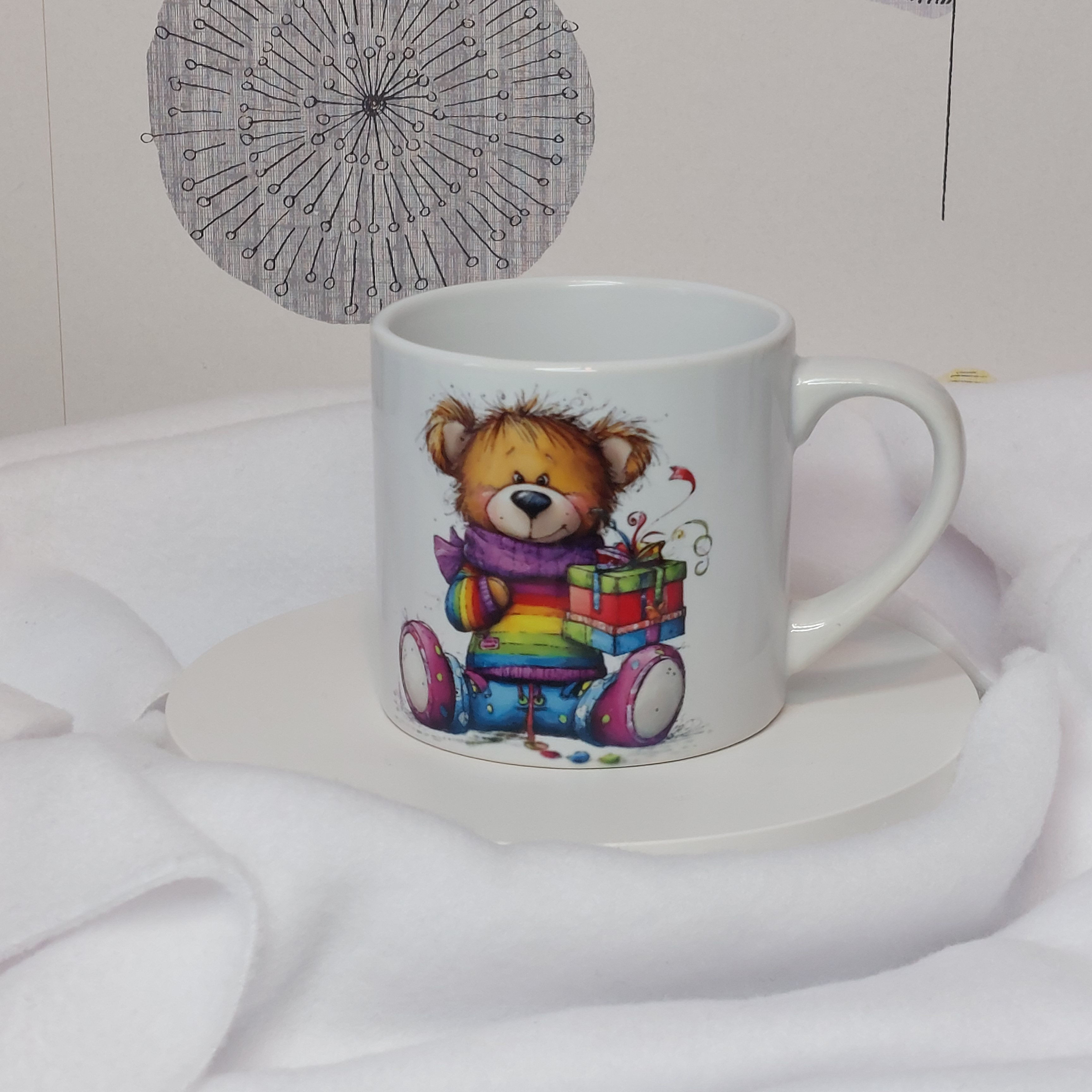 White 6oz ceramic mug with colourful, cute teddy bear in a rainbow jumper  with scarf and holding a stack of presents