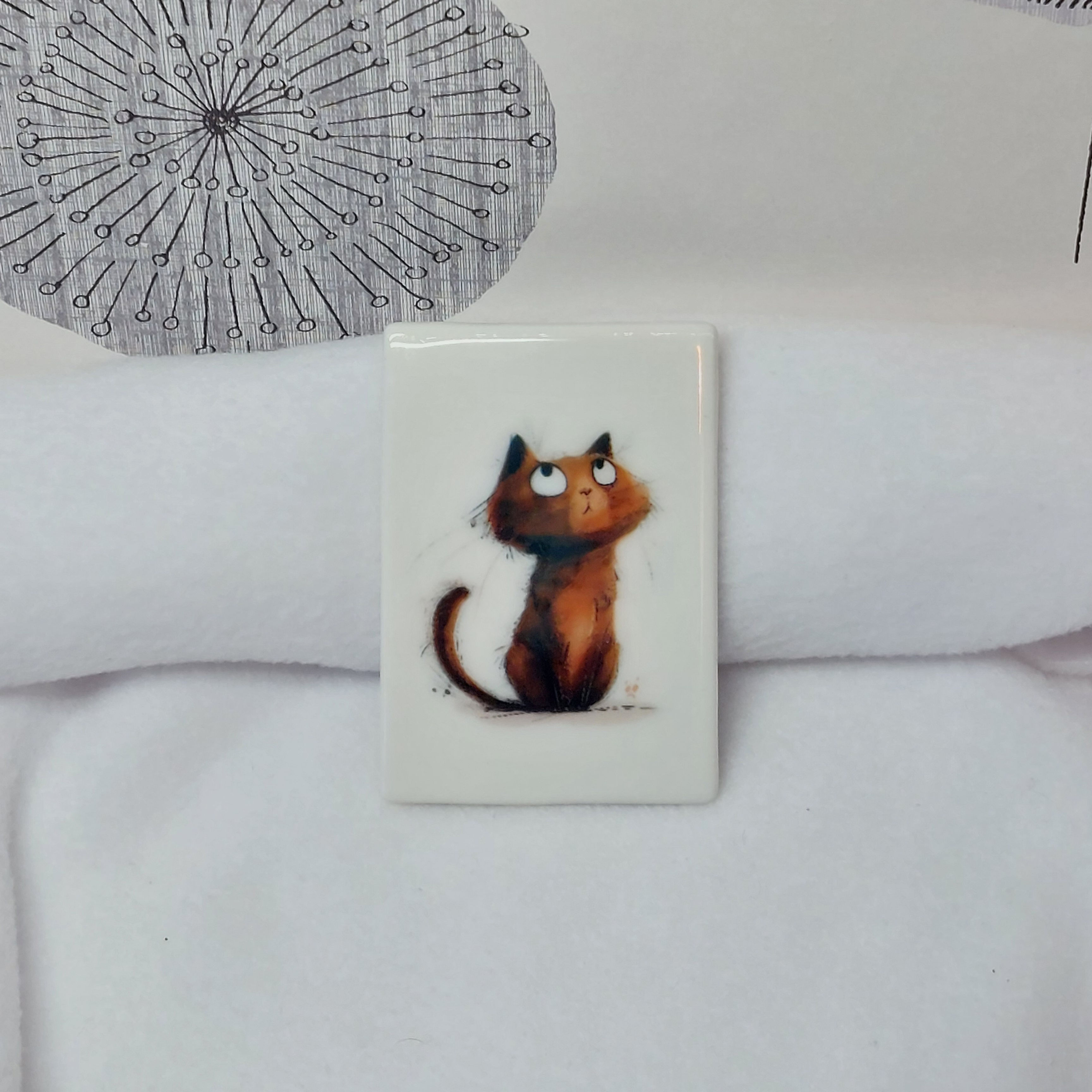 Cartoon painted brown eyerolling cat with whispy hairs and whiskers on a rectangular ceramic magnet