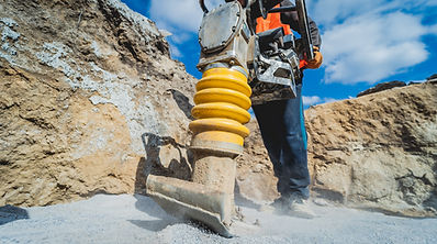 Worker uses a portable vibration rammer at construction of a power transmission substation