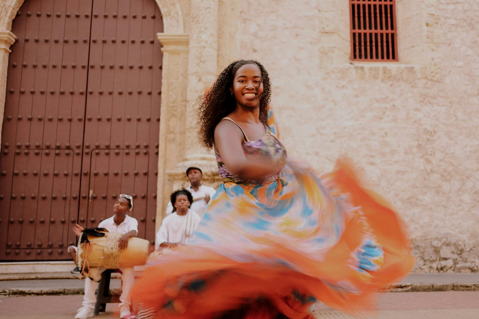 Woman dancing in colorful dress, smiling, with musicians playing in front of a brown, arched door. Joyful ambiance with motion blur.
