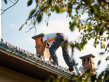 Roofer wearing safety helmet working on fixing tiles on house roof near brick chimneys