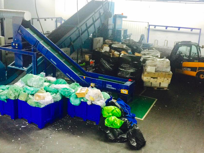 Containers of waste bags beside conveyor belt machinery for shredding