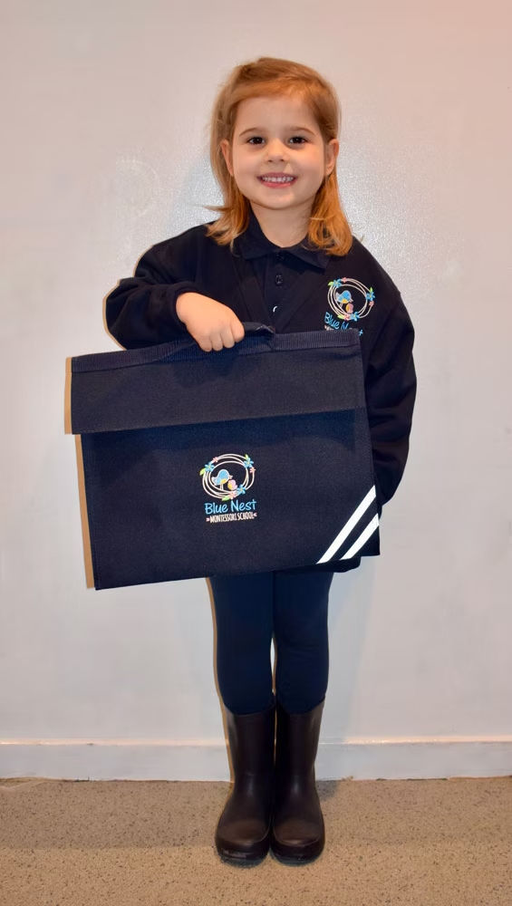 Smiling girl in Blue Nest Montessori uniform holding school book bag