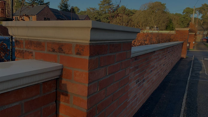 Brick boundary wall with stone coping, a clear blue sky in the background.