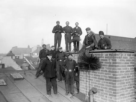 Black and white photo of chimney sweeps and workers posing on a rooftop with brick chimney, early 20th century