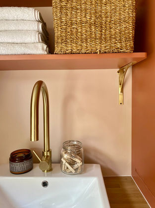 Renovated utility room with coral-painted cabinetry, soft pink walls, new sink and tap, and open shelves with baskets.
