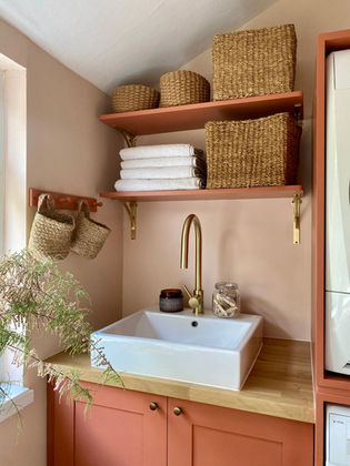 Renovated utility room with coral-painted cabinetry, soft pink walls, new sink and tap, and open shelves with baskets.