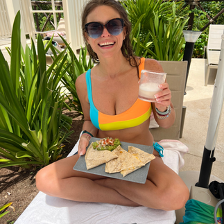 A girl smiling holding quesadillas and a margarita by the pool in a bikini.