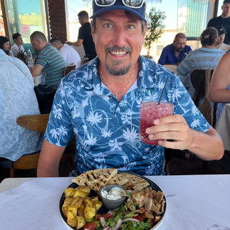 man holding a drink with a plate of greek food in front of him in Santorini