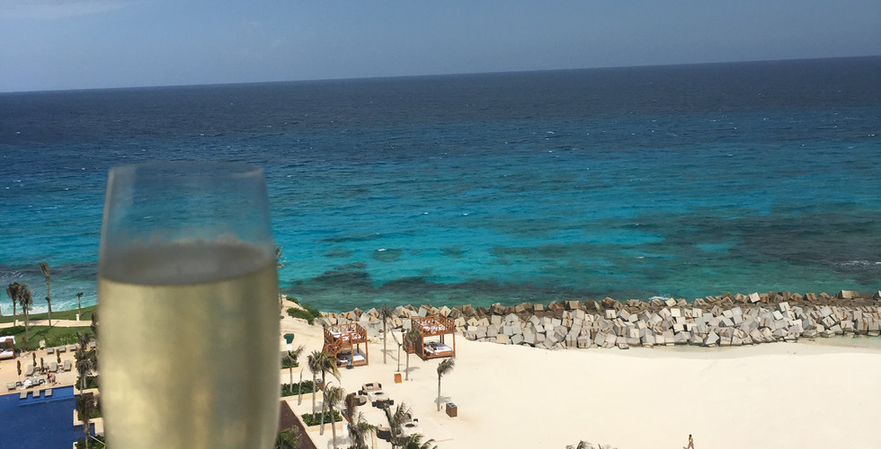 A glass of champagne in the foreground with the viewer looking at the blue caribbean sea and white sand at Hyatt Ziva Cancun