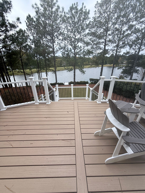 Wooden deck with railing overlooking a lake and trees in background.