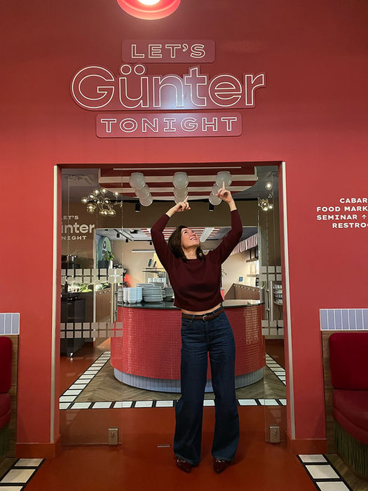 Xenia steht vor dem Logo eines Restaurants, welches den Namen "Günter" trägt.