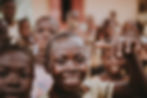 Young boy in Sub-Saharan Africa smiles at camera, surrounded by group of other children