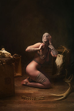 Une femme le visage bandé regarde vers le haut, elle a derrière elle un décor de crâne d'animaux, perte d'identité, recherche de soi