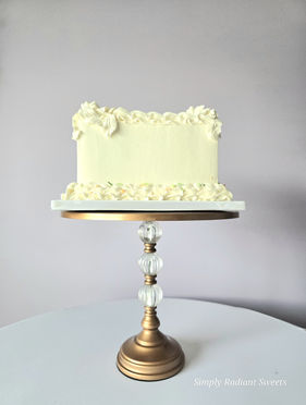 Cream colored cake on a gold stand. Simply Radiant Sweets LLC