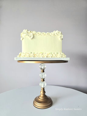 Cream colored cake on a gold stand. Simply Radiant Sweets LLC