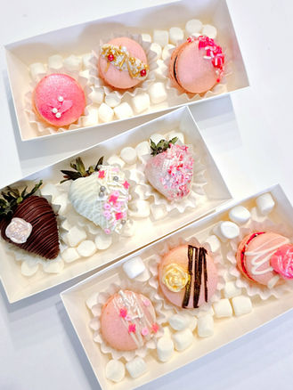 Pink macarons, chocolate-covered strawberries, and other sweets in white boxes. Simply Radiant Sweets LLC