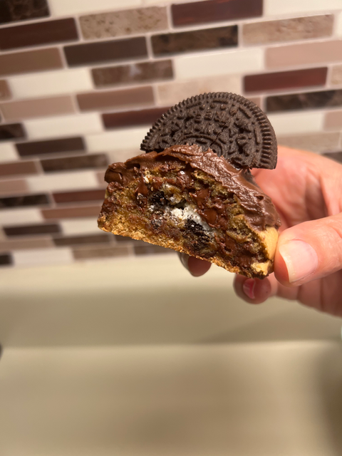Hand holding half of cookie with Oreo and chocolate frosting, Divine Dough.