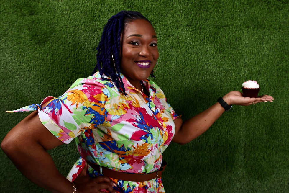 Serene in a colorful floral shirt holds a cupcake against a green textured background.