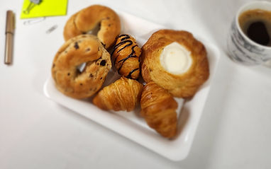 Assortment of pastries on a white tray, including bagels and croissants. Simply Radiant Sweets LLC.