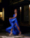 Smiling woman in flowing blue gown with high slit, posing