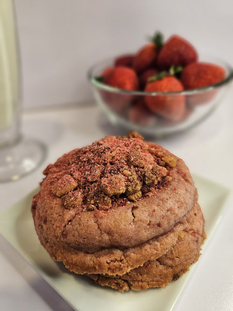 Chocolate cookie on a plate with strawberries in a bowl beside.