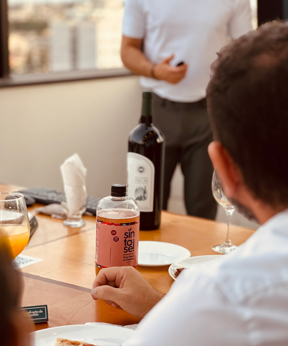 Participantes da Confraria de Gestão da Conexões de Negócio acompanhando apresentação em rooftop, com vinho e bebidas à mesa em ambiente de troca e networking