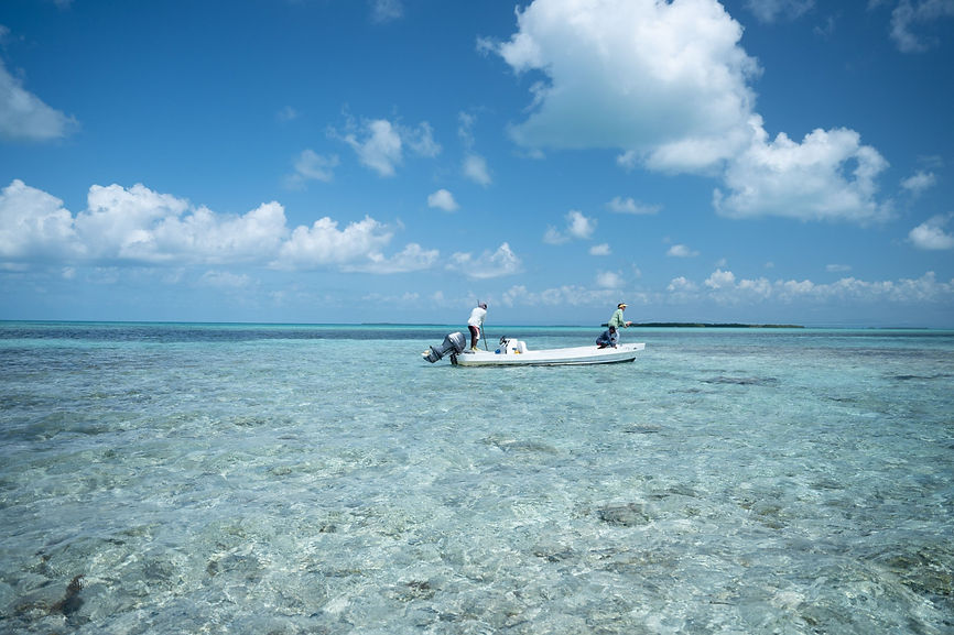 A fly fisher stands on a boat over the Belize Barrier Reef with an island in the distance