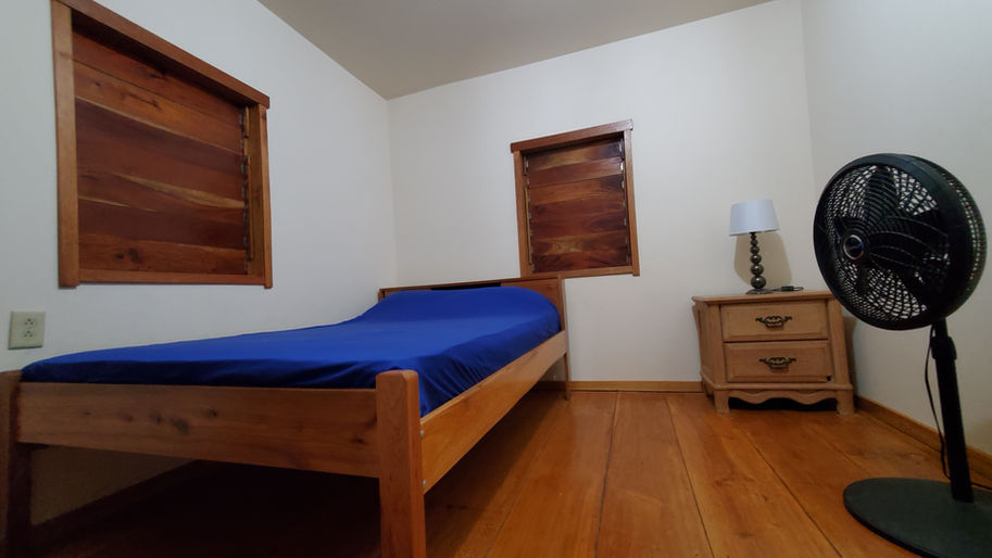 Clean bedroom with wooden bed, blue sheet, nightstand, and lamp