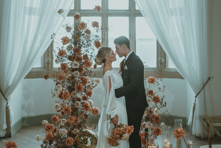 A couple stand in front of some orange and brown flowers